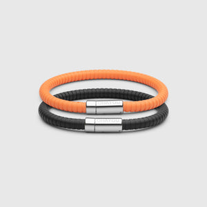 The Signature Bracelet in black with stainless steel clasp. FKM fluoroelastomer rubber – Fully waterproof. Bundled together with the Signature Bracelet in orange on white background.