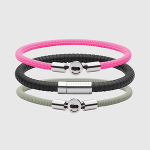 The Signature Bracelet in black with stainless steel clasp. FKM fluoroelastomer rubber – Fully waterproof. Bundled together with the Smile Bracelet in Neon Pink and Light Green in silicon rubber, and White background.