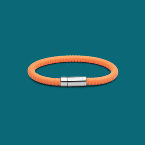 The Signature Bracelet in orange with stainless steel clasp. FKM fluoroelastomer rubber – Fully waterproof. Blue/Green background.